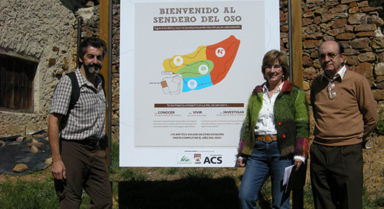 Tres integrantes de la Fundación Oso Pardo delante de un cartel de la Senda del Oso en Verdeña, Palencia