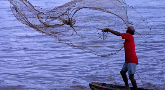 Un pescador lanzando la red al agua desde su pequeña embarcación
