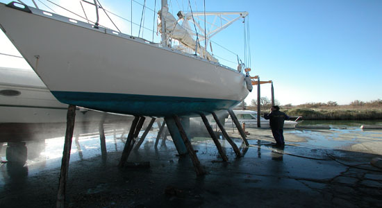 Un trabajador limpiando con agua a presión el casco de un velero en dique seco