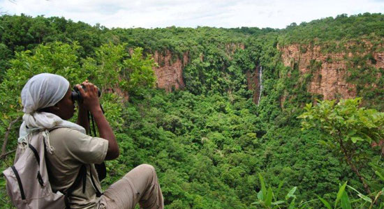 Una cooperante local observa la Cascada de Dindefelo con los prismáticos en Kedougou, Senegal