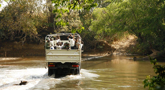 Un grupo de visitantes en un camión vadeando un río del Parque